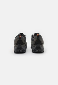 Dunkelgraue Sneakers mit einer Kombination aus Wildleder und Mesh-Materialien, ausgestattet mit einer strukturierten schwarzen Sohle und orangen Logoakzenten an der Ferse.