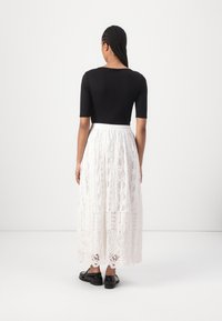 Zwarte top met korte mouwen, gecombineerd met een lange witte kanten rok met ingewikkelde patronen en een geplooide tailleband, gedragen met zwarte schoenen.