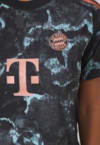 Musta ja turkoosi sidotut T-paita, jossa on suuri vaaleanpunainen Telekom-logo ja FC Bayern Münchenin merkki. Pyöreä kaula-aukko.