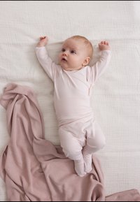 Lys rosa langermet romper på en baby med hevede armer, som ligger på teksturert hvit stoff, ved siden av et rosa strikket teppe.