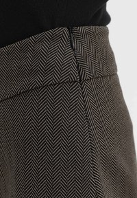 Jupe taille haute avec motif chevrons noir et beige et fermeture éclair latérale, portée avec un top noir.