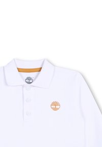 Witte polo met een drieknops sluiting, textuurstof en een klein oranje boomlogo op de linkerborst. Klassieke kraag.