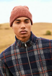 Rote gerippte Mütze und navyfarbene Fleecejacke mit Karomuster in Grau und Rot. Die Jacke hat einen Reißverschluss und ein hohes Kragen-Design.