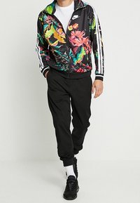 Svarta träningsbyxor med elastiska muddar, kombinerade med en svart zip-jacka med ett livligt blommönster och vita sidskåror.