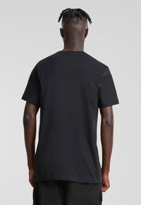 Czarny t-shirt z krótkim rękawem wykonany z gładkiej bawełnianej tkaniny, z okrągłym dekoltem i luźnym krojem, bez widocznych wzorów ani ozdób.