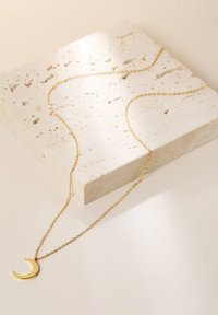 Collier en chaîne en oravec un pendentif en forme de croissant de lune, posé sur une surface en pierre claire texturée, mettant en valeur son fini brillant et son design délicat.