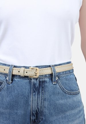 Beige leather belt with gold studs, featuring a metal buckle, worn over blue high-waisted jeans and a white sleeveless top.
