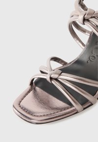 Metallisk rosaguld sandaler med korsande remmar och en kvadratisk tåsdesign. Slät textur med minimalistisk detaljering och en svart innersula.
