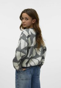 Pull en laine gris avec des motifs géométriques blancs, avec un col rond et une coupe ample. Associé à un jean en denim bleu taille haute.