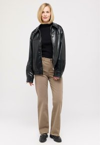 Schwarze Leder-Übergröße-Jacke, eng anliegender schwarzer Pullover, beigefarbene weit geschnittene Hose und schwarze Schuhe mit Hardware-Akzenten. Glatte Textur, lässiges Design.