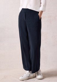 Marineblauwe wijde broek gemaakt van zachte stof, met zijzakken en een gladde textuur, gecombineerd met witte sneakers.