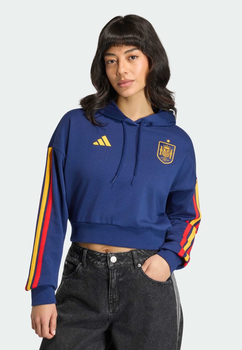 Blauer gekürzter Hoodie mit Kapuze und Fronttasche, mit gelbem Adidas-Logo und Wappen. Rote und gelbe Streifen entlang der Ärmel.