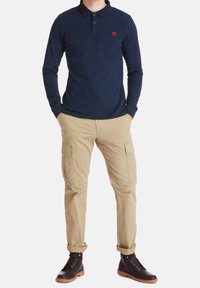 Mörkblå långärmad polo med en liten röd logotyp, matchad med ljus khaki cargobyxor och bruna snörskor. Avslappnad design med fickor.