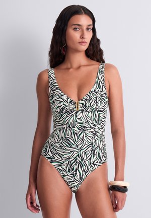 Femme portant un maillot de bain une-pièce imprimé zèbre en noir, blanc et vert, avec une fermeture dorée et deux bracelets à son poignet droit.