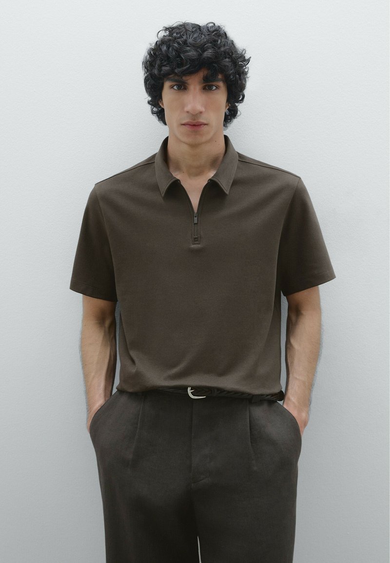 Polo shirt marrone con design a metà zip, maniche corte e una texture liscia, abbinato a pantaloni scuri e una cintura con una fibbia semplice.