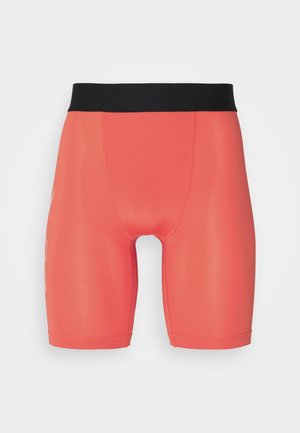 Obcisłe, koralowe spodenki sportowe z wysokim, czarnym pasem, sięgające do połowy uda, na jednolitym, białym tle.