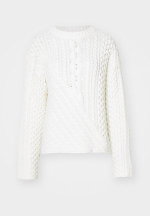 Suéter blanco de punto con un patrón de cable texturizado, cuello redondo y mangas largas. El diseño incluye una sección frontal diagonal.