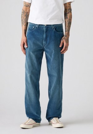 Lichtblauwe denim jeans met een relaxte pasvorm, voorzien van vijf zakken en subtiele verticale ribbels. Gecombineerd met off-white sneakers.