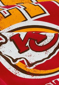 Tela roja con un gráfico audaz de estilo vintage en amarillo y blanco. Logo prominente con textura desgastada y elementos de diseño curvados.