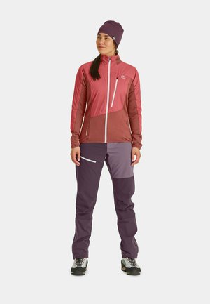 Outdoor-Jacke in Rosatönen mit Reißverschluss vorne, kombiniert mit dunkelvioletten Hosen mit Seitentaschen und kontrastierenden Einsätzen.