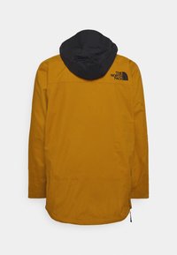 Veste jaune avec capuche noire et logo "The North Face" en haut à droite du dos, vue de dos sur fond uni.