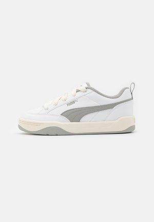 Sneakers PUMA bianchi e grigi, caratterizzati da una tomaia in pelle liscia, suola bianca spessa e striscia laterale grigia. Lacci e dettagli della linguetta color crema.
