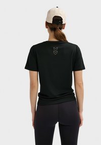 Svart tränings t-shirt med korta ärmar, med en slät yta och en liten vit chevron-grafik i mitten på ryggen.