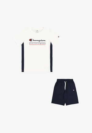 Maglietta sportiva bianca con pannelli laterali blu e testo grafico rosso "Champion", abbinata a pantaloni corti blu con vita elastica.