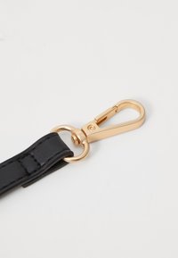 Sort læderrem med guldfarvet metalclips, der har en cirkulær ring og struktureret finish. Kompakt design, der er velegnet til sikker fastgørelse.