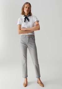 Jeans in denim grigio con vita alta, design a gamba dritta e orli arrotolati, abbinati a una camicia bianca a maniche corte e a una sciarpa a motivi.