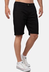 Shorts en coton noir mélangé avec des revers roulés, fermeture à bouton classique et poches latérales, associés à des baskets blanches.