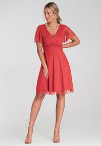 Rotes Kleid mit tailliertem Oberteil und A-Linie-Rock. Mit transparenten, schwingenden Ärmeln und einem V-Ausschnitt. Glattes Material mit fließender Textur.