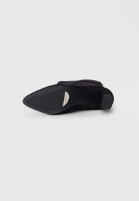 Black high-heeled shoe with a pointed toe and suede upper. Features a smooth rubber outsole and a small metallic logo detail on the side.