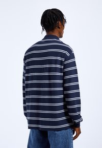 Navy and white striped long-sleeve shirt with a collared neckline and textured fabric. The design features a relaxed fit and side slits.