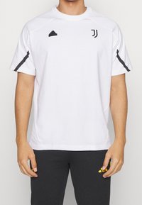 Biała koszulka sportowa z czarnymi akcentami, prążkowany dekolt w serek oraz detal z logo. Krótkie rękawy i luźny krój. Miękka, oddychająca tkanina.