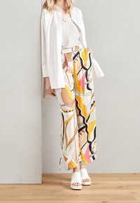 Färgglada vida byxor med ett djärvt abstrakt mönster av vågiga linjer i rosa, gult och grönt; kombinerat med en vit skjorta med knappar och vita skor.