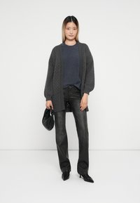 Oversized grå strikket cardigan, mørkeblå topp, svarte jeans og spisse svarte hæler. Modellen holder en svart veske, med et strukturert mønster på cardiganen.
