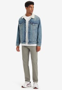Chaqueta de denim con un lavado en azul claro y cuello de borreguito blanco, combinada con una camiseta blanca y pantalones gris claro. Incluye zapatillas blancas.