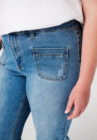 Jean en denim bleu clair avec taille haute, design à cinq poches, légères décolorations et détails de couture contrastants.