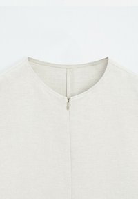 Light beige top made from textured fabric, featuring a round neckline and a back zipper closure. Simple, clean design without patterns.