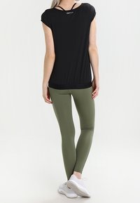 Top atlético negro de manga corta con dobladillo redondeado, combinado con leggings verde oliva. El conjunto tiene una textura suave y presenta un mínimo de marcas.