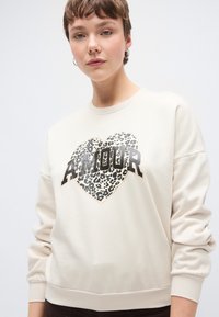 Φούτερ κρεμ με σχέδιο καρδιάς σε λεοπάρ σχέδιο και τη λέξη "AMOUR" με έντονα μαύρα γράμματα. Ριμπ μανσέτες και τελείωμα.