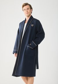 Marineblauer Bademantel mit Waffelstruktur, Schalkragen, cremefarbener Paspel und gesticktem Logo. Verfügt über zwei vordere Taschen und einen selbstbindenden Gürtel.