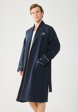 Navy waffle-textured robe with a shawl collar, cream piping, and an embroidered logo. Features two front pockets and a self-tie belt.