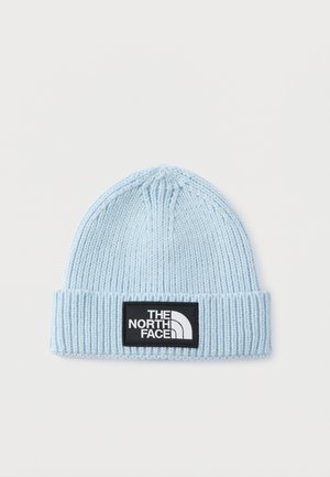 Svetlo modra pletena kapa z rebrasto teksturo, podvitim robom in črnim pravokotnim oznako z logotipom "THE NORTH FACE" v belem.