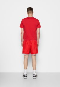 Czerwona bawełniana koszulka i czerwone satynowe szorty z białym wykończeniem, widok z tyłu. Czarno-białe sneakersy w wzory, białe skarpetki.