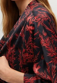 Tissu noir fluide avec motif de feuilles rouges ; design ample avec manches larges, mettant en valeur une texture naturelle et un tombé léger.