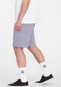 Hellgraue Shorts in einer lockeren Passform, aus flexiblem Material. Mit einem einfachen Saum gestaltet, getragen mit schwarzen Sneakern und weißen Socken mit Logo.