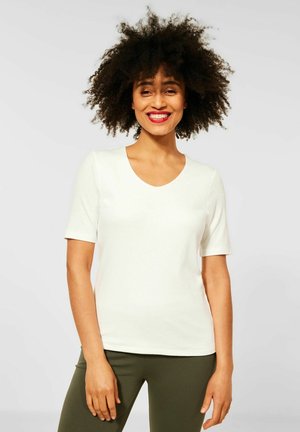 Bílý krátký rukáv v-neck tričko vyrobené z měkké tkaniny, spárované se zelenými legínami. Hladká textura s dobře padnoucím designem.