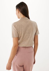 Krátký rukáv béžový pletený top s vysokým límcem, v kombinaci s světle růžovými kalhotami na míru s zadními kapsami a jemnými švy.